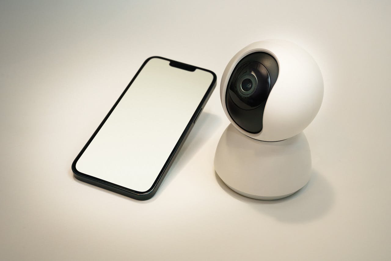 about-01 A modern smart home security camera next to a blank screen smartphone, showcasing home automation technology.