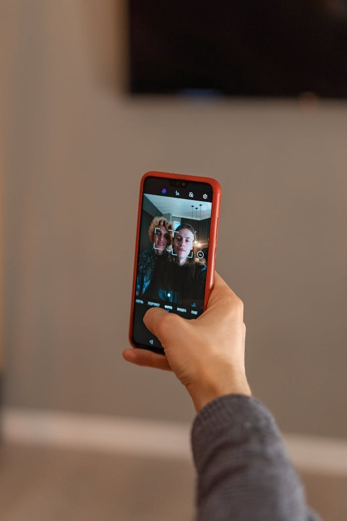 services-02 Person holding a smartphone capturing a group selfie at home.
